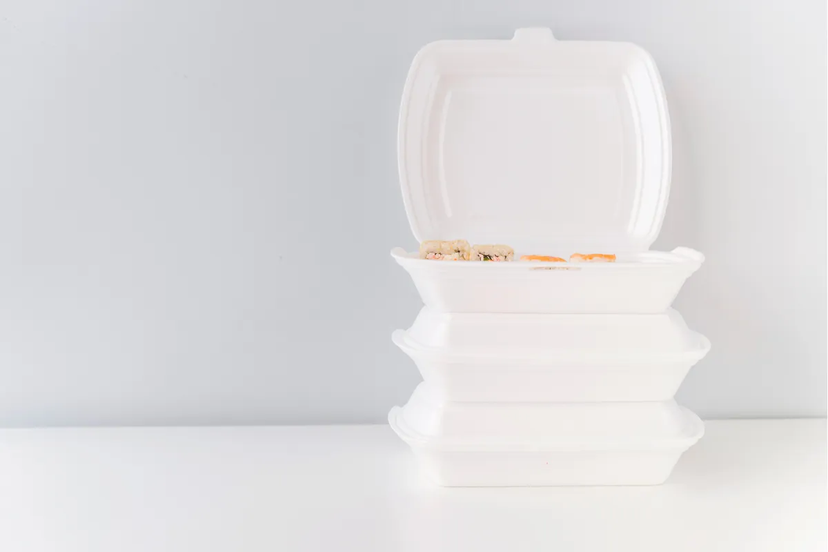 Marmitas de isopor empilhadas, com a tampa superior aberta mostrando alimentos dentro, ilustrando embalagens leves e acessíveis usadas para refeições quentes em deliveries populares.