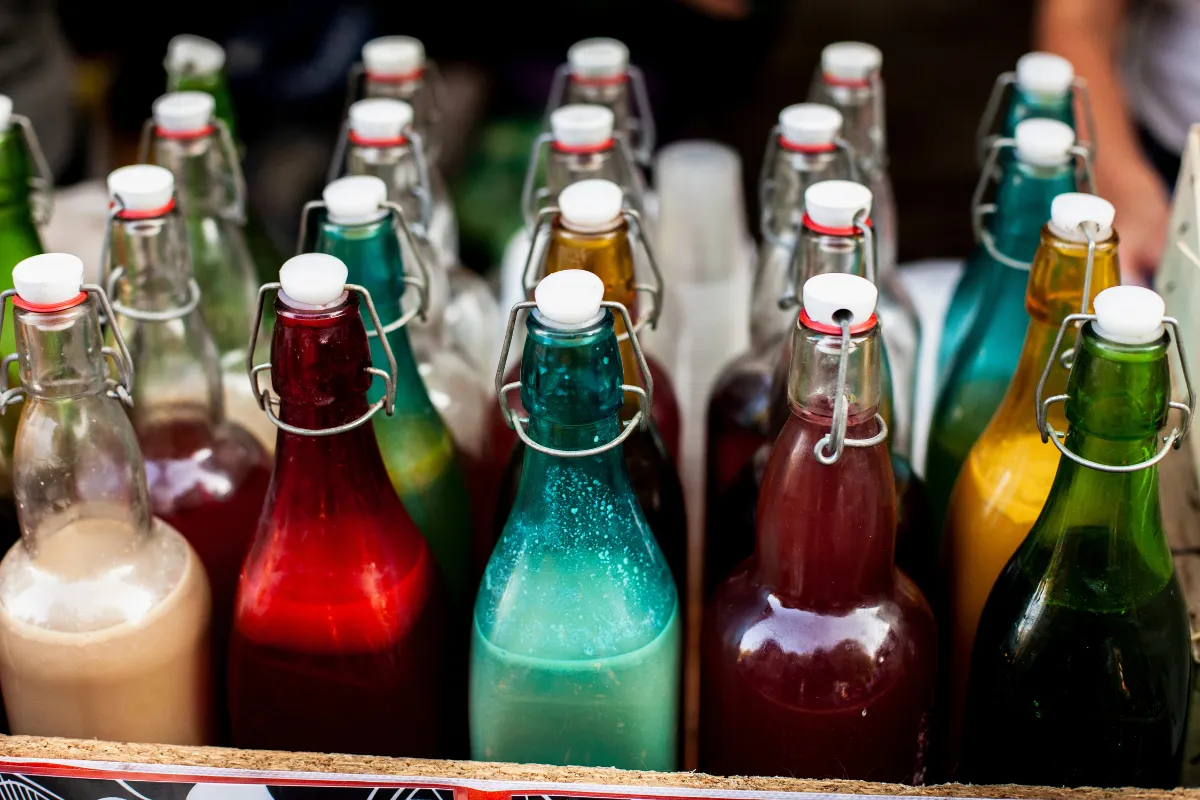 Diversas garrafas coloridas sem rótulo, exemplificando o risco ao não verificar a segurança e procedência das bebidas e a importância de escolher uma distribuidora confiável para evitar produtos adulterados.