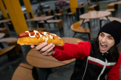 Cliente satisfeito segurando hot dog com salsicha e maionese em lanchonete, demonstrando experiência positiva no delivery