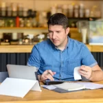 Empreendedor de Food Service revisando contas e usando uma calculadora e um tablet, ilustrando a necessidade de revisão de preços e adaptação dos sistemas de gestão para o IVA.