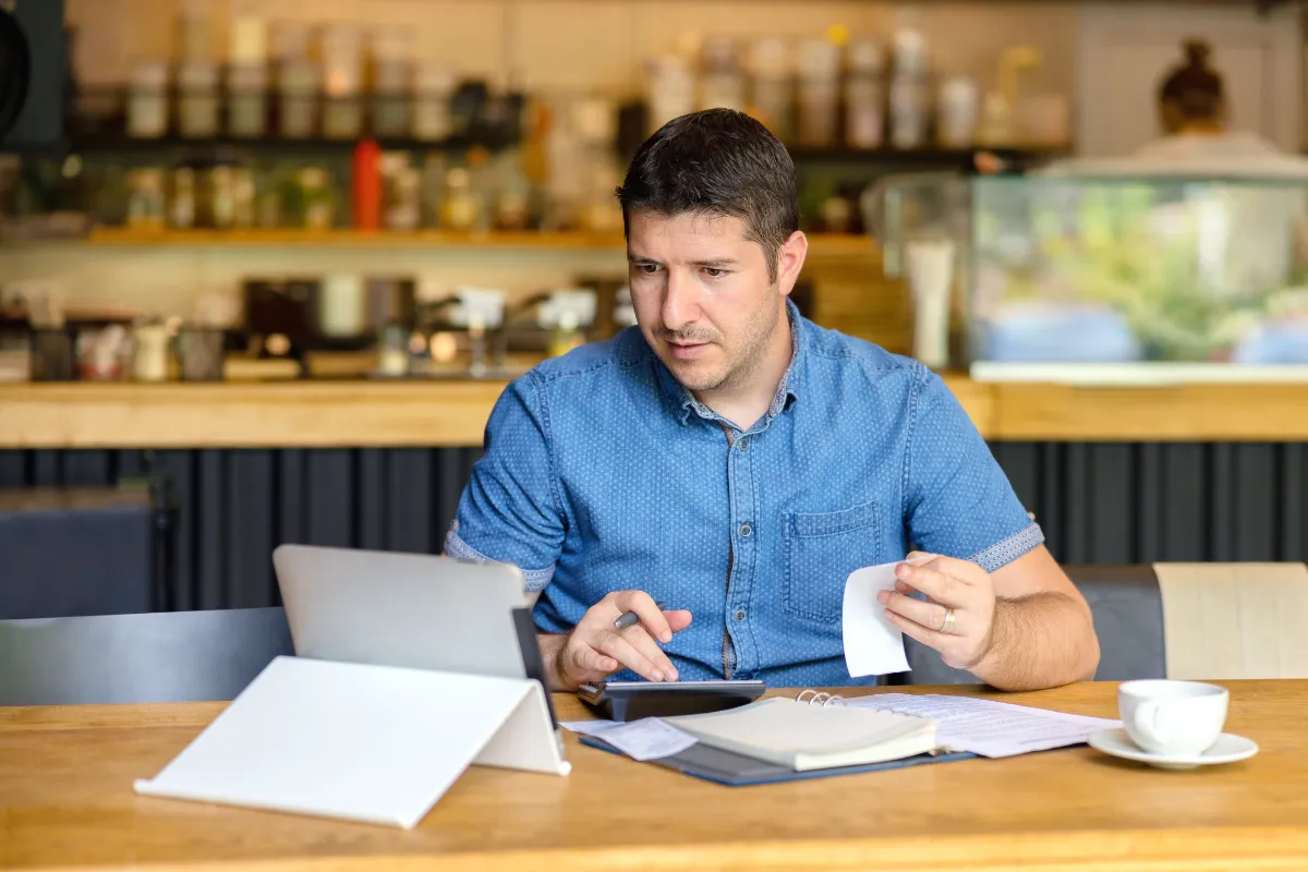 Empreendedor de Food Service revisando contas e usando uma calculadora e um tablet, ilustrando a necessidade de revisão de preços e adaptação dos sistemas de gestão para o IVA.