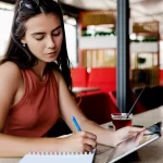 Gestora de restaurante calculando custos e markup em caderno enquanto usa tablet para análise financeira do cardápio