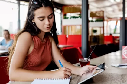 Gestora de restaurante calculando custos e markup em caderno enquanto usa tablet para análise financeira do cardápio