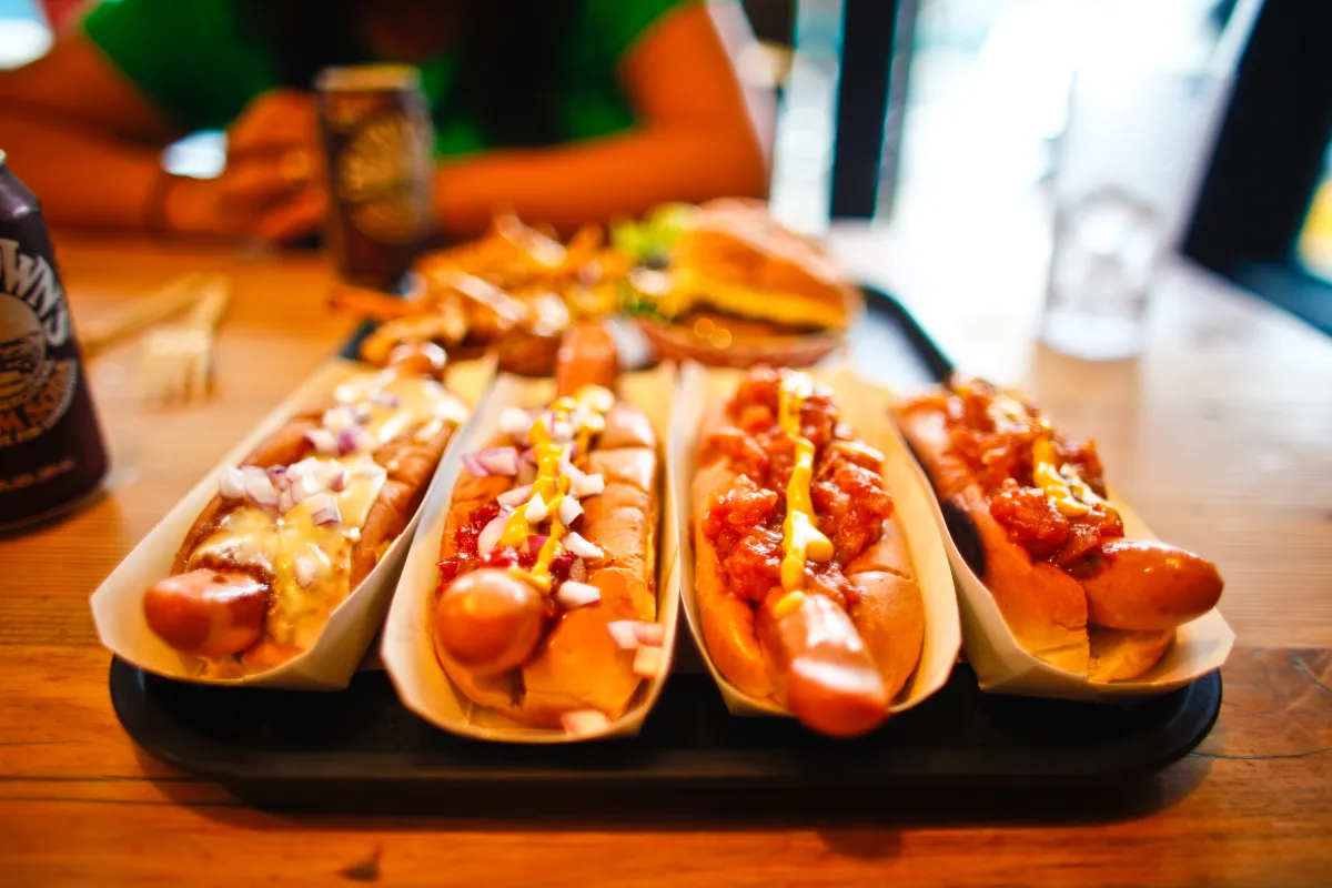 Bandeja com quatro hot dogs variados com coberturas diferentes em mesa de restaurante, mostrando diversidade de cardápio