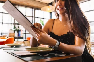 Cliente sorridente escolhe prato em cardápio físico, destacando a importância do menu na etapa de decisão da jornada do cliente em restaurante.