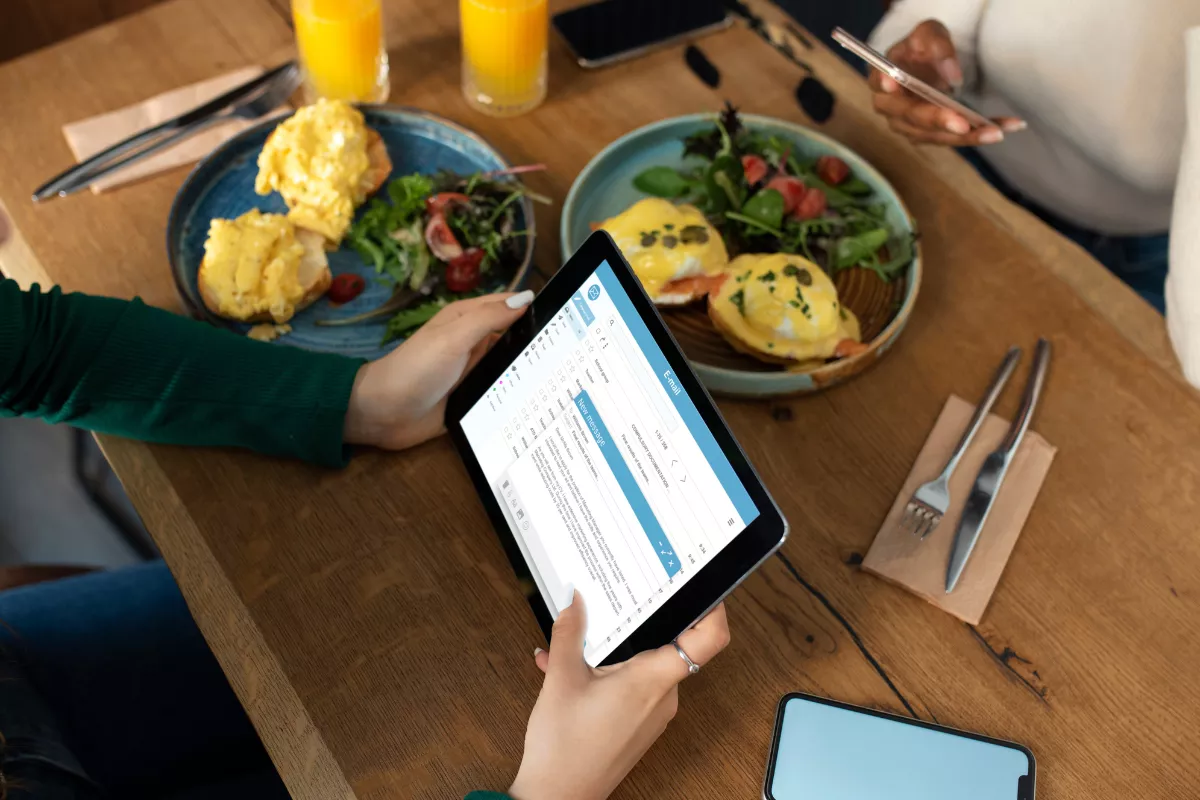 Clientes em uma mesa de restaurante com pratos servidos, analisando o cardápio ou pesquisas de satisfação em um tablet. O foco é a estratégia para aumentar o Ticket Médio, um KPI crucial entre os indicadores de desempenho restaurantes.