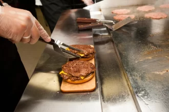 Profissional preparando cheeseburgers na Chapa Tradicional. A superfície lisa permite selar o pão e preparar diversos acompanhamentos ao mesmo tempo.
