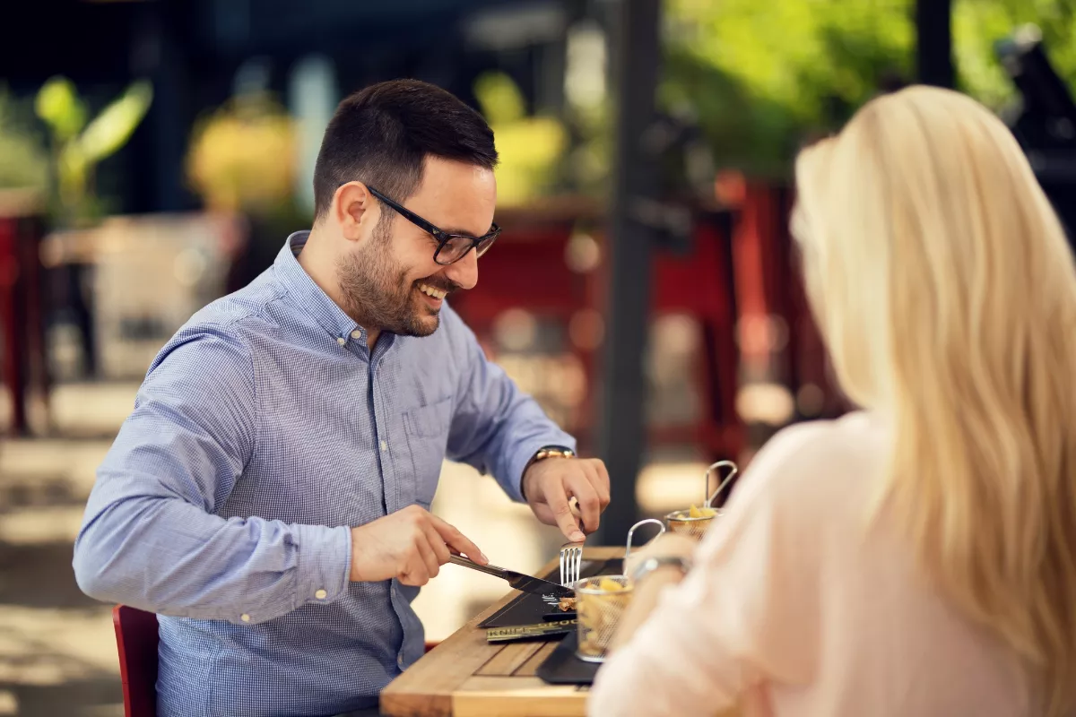 Casal sorrindo e desfrutando da refeição em um restaurante, simbolizando a satisfação e a fidelização do cliente.