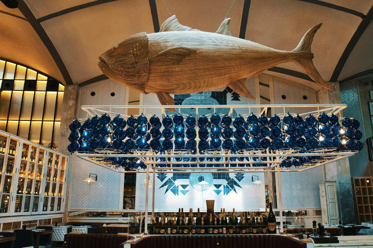 Ambiente interno de restaurante temático de peixes, com grande escultura de peixe pendurada no teto, simbolizando a importância de ambientes bem organizados e sistemas de gestão otimizados no segmento de pesque e pague.