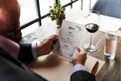Visão superior de um homem em um terno lendo um cardápio de design elegante com o título 'Menu' e divisões como 'Starter', 'Main' e 'Dessert', ao lado de uma taça de vinho tinto e um copo d'água. A imagem destaca a apresentação de um menu degustação e a sofisticação da experiência, conectando-se à seção do texto que explica o conceito de 'tour gastronômico' e a desmistificação de que esse menu não é exclusivo de restaurantes de luxo