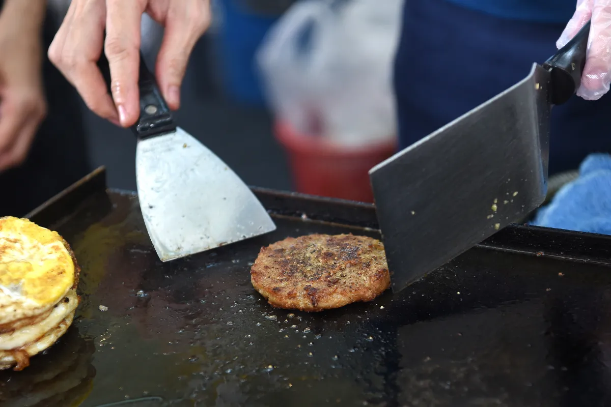 Processo de preparo de um "smash burger" em uma chapa lisa. A chapa é um equipamento essencial para padronização e agilidade na cozinha.
