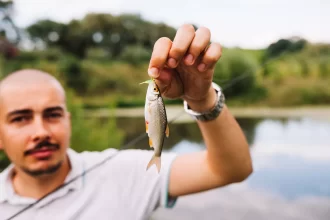 Homem segurando um pequeno peixe recém-pescado, à beira de um lago em um pesque e pague, ilustrando a experiência do cliente nesse tipo de estabelecimento e a importância de registrar e pesar cada pescado de forma eficiente.