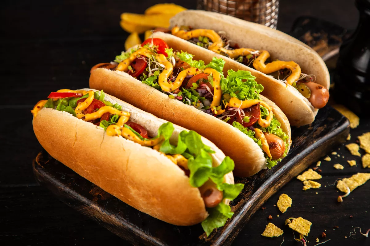 Três cachorros-quentes artesanais com molhos e folhas verdes, representando a variedade de cardápios para aumentar o lucro em carrinho de cachorro-quente