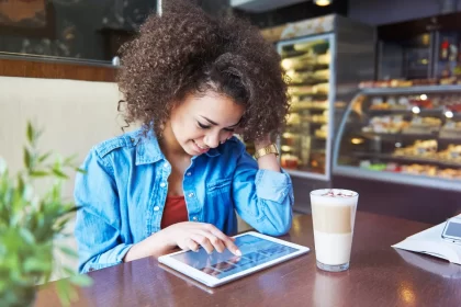 ovem sorridente em cafeteria utilizando um tablet sobre a mesa para navegar pelo cardápio digital, ilustrando a autonomia e facilidade que a tecnologia proporciona na escolha do pedido em restaurantes e cafés.