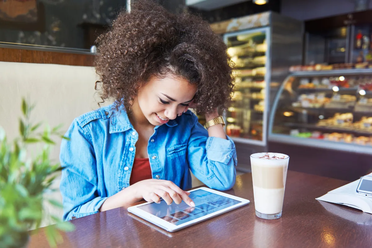 ovem sorridente em cafeteria utilizando um tablet sobre a mesa para navegar pelo cardápio digital, ilustrando a autonomia e facilidade que a tecnologia proporciona na escolha do pedido em restaurantes e cafés.