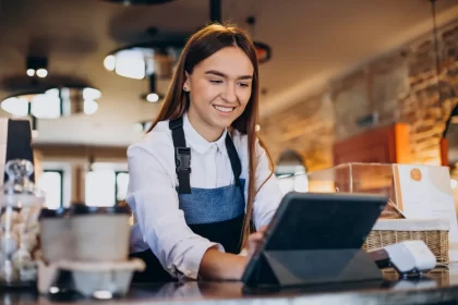 Atendente de cafeteria sorrindo ao usar um tablet como frente de caixa intuitivo para registrar pedidos, ilustrando a facilidade de uso e modernização do atendimento com o sistema CNM.