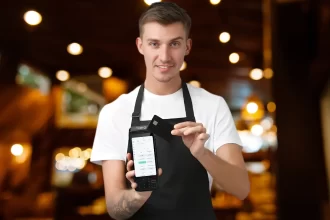 Garçom em ambiente de restaurante segurando uma maquininha Cielo Lio integrada ao sistema PDV do CNM, demonstrando a agilidade do atendimento e pagamento móvel na mesa do cliente