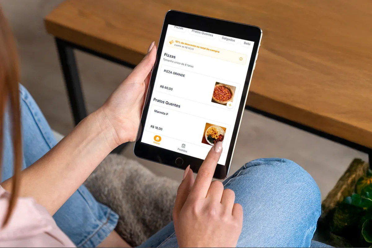 Cliente sentado usando um tablet para fazer um pedido pelo cardápio digital diretamente na mesa do restaurante, escolhendo itens e aproveitando descontos de forma prática e rápida.