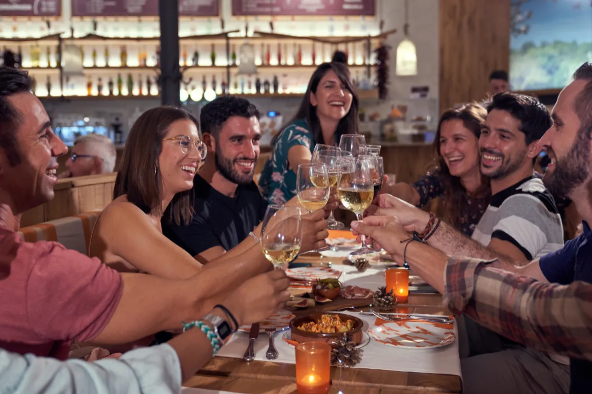 Grupo de amigos sorrindo e brindando com taças de vinho em uma mesa de restaurante, representando a celebração do Dia da Amizade em fevereiro.
