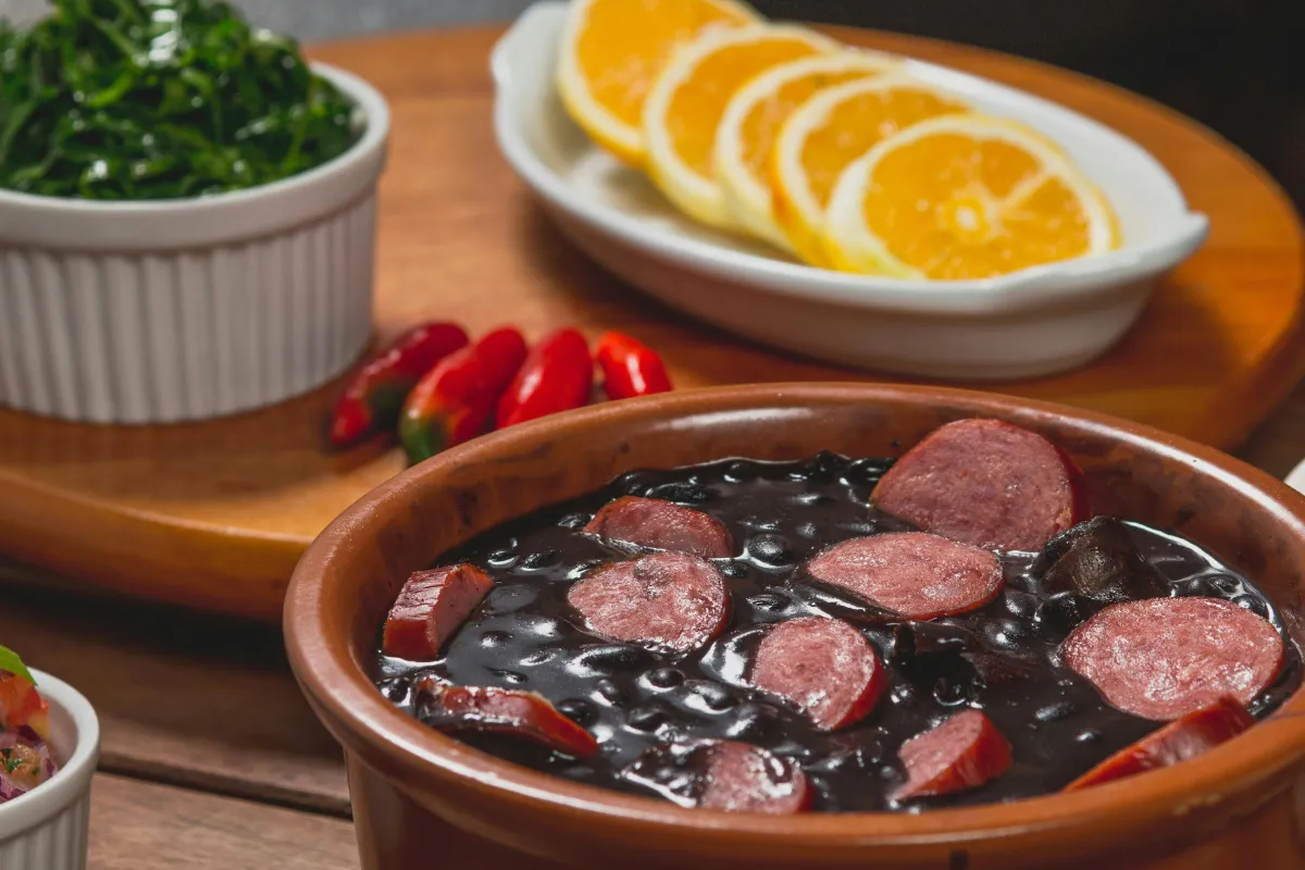 Prato de feijoada brasileira tradicional em cumbuca de barro, acompanhada de couve, laranja e pimenta, conectando a gastronomia típica ao Dia da Consciência Negra em novembro.
