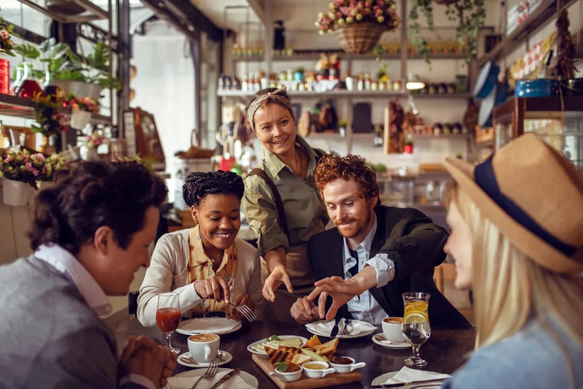 Garçonete servindo e interagindo com um grupo diversificado de clientes felizes à mesa, simbolizando a hospitalidade e o foco no Dia do Cliente em setembro.