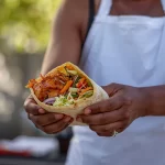 Pessoa segurando um wrap vegano recheado com vegetais coloridos, uma opção de lanche prático e saudável no delivery.
