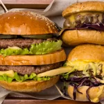 Caixa de madeira contendo quatro hambúrgueres artesanais de sabores variados, ideal para delivery e grupos, representando a ideia de Combo Box Experience para hamburguerias.