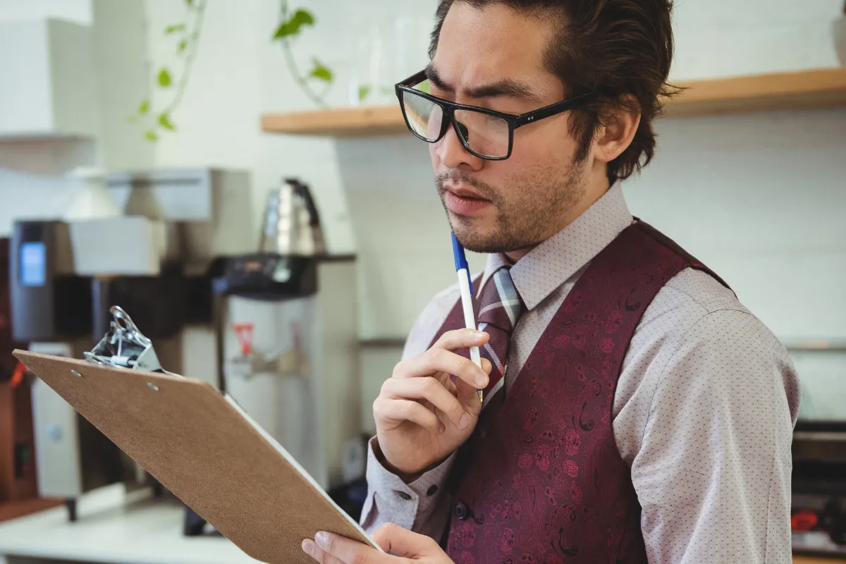Gestor de restaurante analisando prancheta com expressão de preocupação ao tentar calcular o CMV (Custo de Mercadoria Vendida) manualmente.
