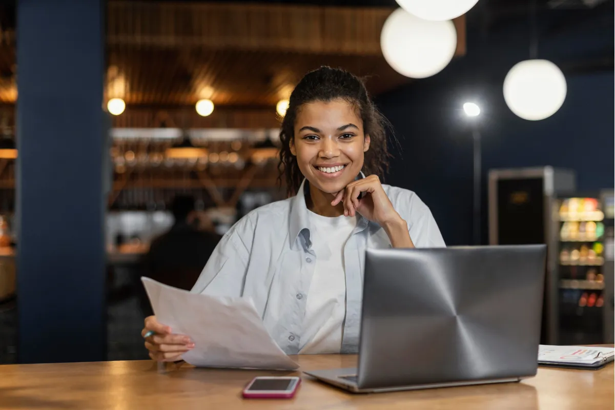 Mulher gestora de restaurante sorrindo enquanto trabalha no laptop, confiante com a gestão fiscal automatizada do seu negócio.