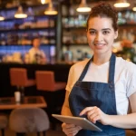Gerente ou garçonete sorrindo segurando um tablet, demonstrando o uso de um sistema ERP para centralizar a gestão do restaurante de forma eficiente.