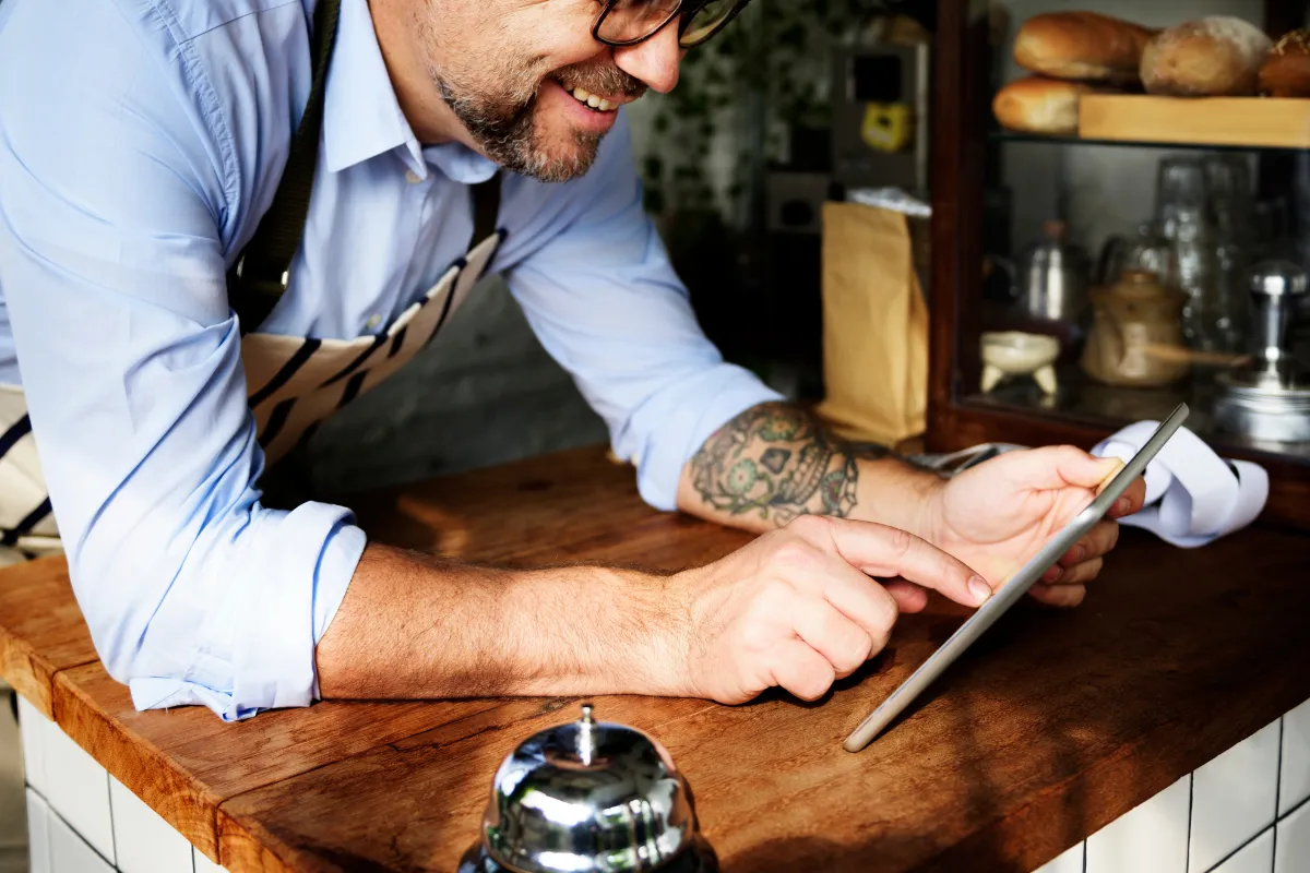 Dono de restaurante sorridente utilizando um tablet para gerenciar seu negócio e consultar informações fiscais com facilidade.
