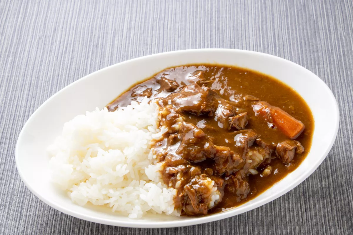 Prato de Karê Raisu, o curry japonês, servido em uma travessa branca. De um lado, arroz branco cozido (gohan) e, do outro, um ensopado de molho marrom espesso com pedaços suculentos de carne e cenoura cozida