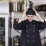 Cozinheiro de doma preta preocupado com o lucro do restaurante, com as mãos na cabeça e o olhar para baixo