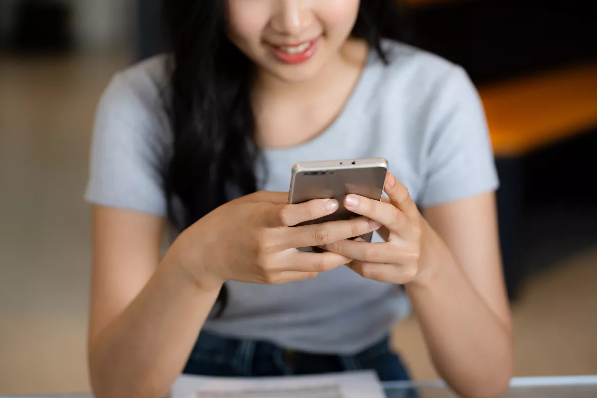 Mulher sorridente utilizando um smartphone para interagir com o atendimento de um estabelecimento. A imagem contextualiza o uso do Chatbot com IA do ControleNaMão, que oferece respostas automáticas e suporte 24/7 via WhatsApp.