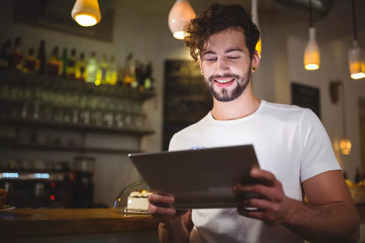 Gestor de restaurante sorrindo ao consultar dados no tablet, representando a facilidade de fazer análises preditivas com o sistema ControleNaMão em um ambiente de bar descontraído.
