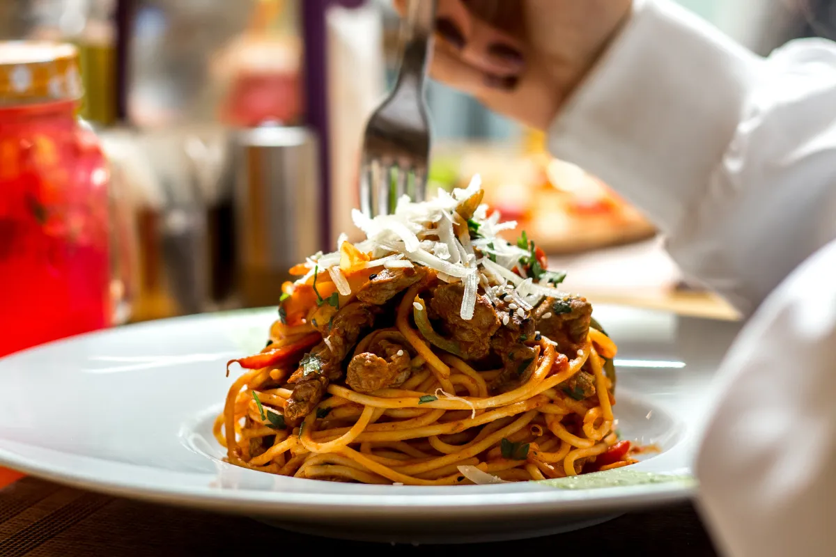 Close-up de um prato de espaguete gourmet com carne, manjericão e queijo parmesão ralado por cima, destacando a apresentação de qualidade para um delivery de massas de sucesso.