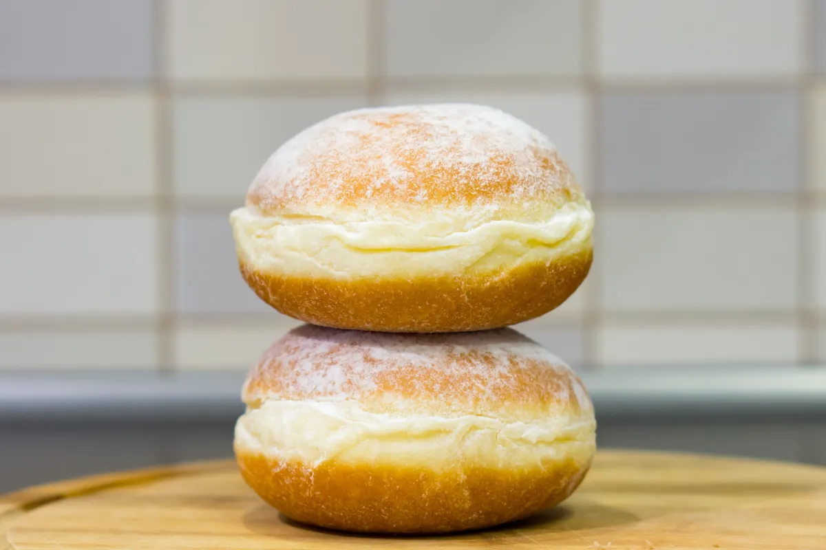 Dois pães doces tradicionais de padaria (estilo sonho ou pão de creme) empilhados, recheados com uma camada generosa de creme branco e polvilhados com açúcar de confeiteiro fino