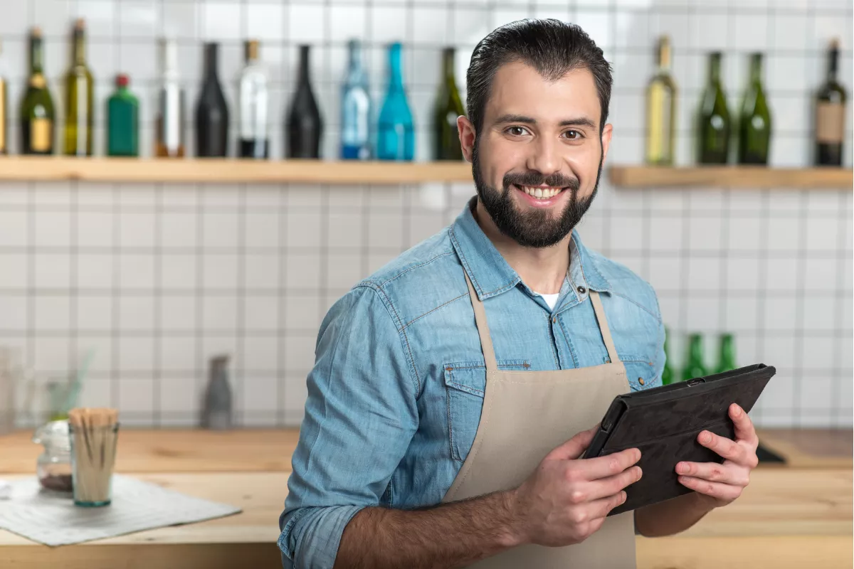 Garçom sorridente segurando um tablet para anotar pedidos em um restaurante, exemplificando a agilidade no atendimento de rodízio com tecnologia.