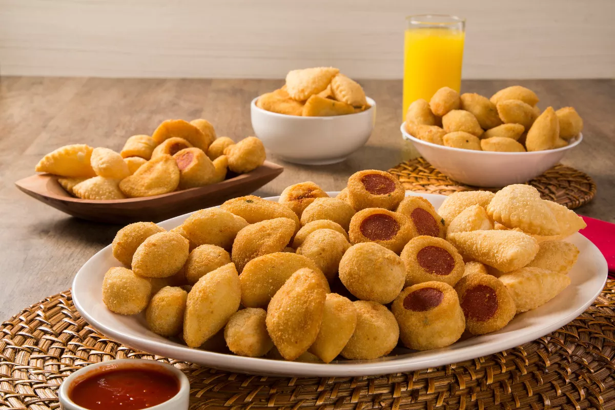 Mesa com porções variadas de salgadinhos fritos como coxinhas, pastéis e bolinhas de queijo, ilustrando o rodízio de petiscos.
