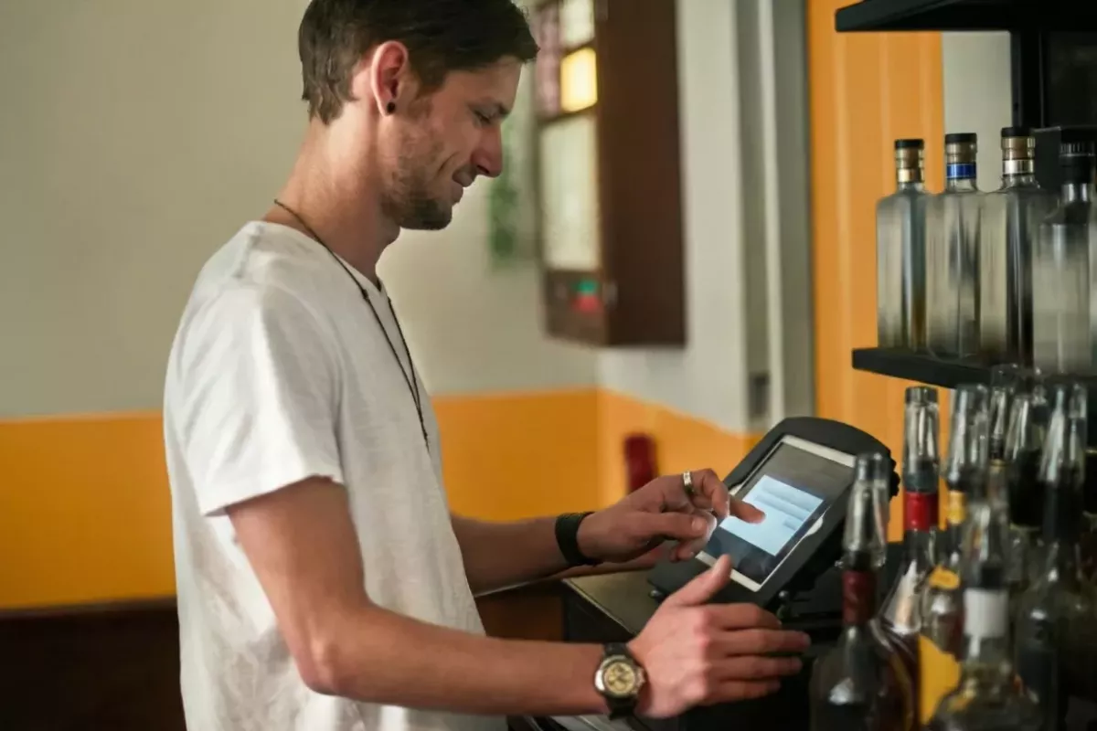 Bartender em um balcão de bar visualizando e gerenciando pedidos em uma tela de Sistema KDS (Kitchen Display System). A imagem demonstra a organização visual dos pedidos por ordem de chegada, substituindo papéis térmicos e otimizando o fluxo de trabalho.