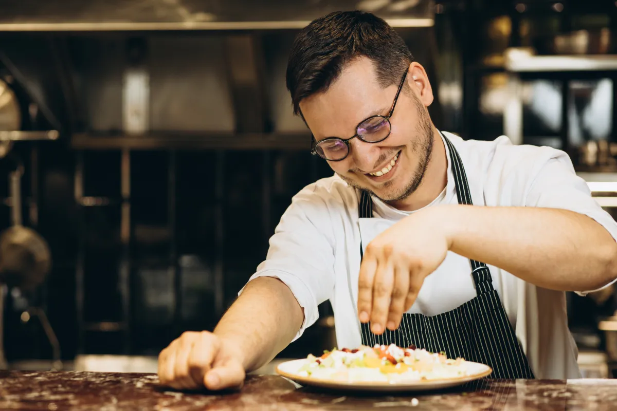Chef de cozinha sorridente finalizando a montagem de um prato gourmet em um balcão de restaurante, demonstrando a eficiência operacional proporcionada por um sistema de automação para restaurantes de macarrão.