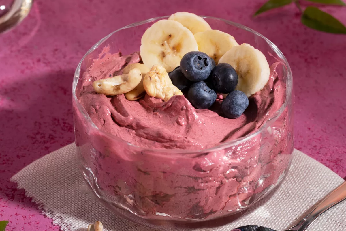 Taça de sobremesa gelada de frutas vermelhas (sorbet ou açaí) decorada com fatias de banana, mirtilos e castanhas. Opção de sobremesa leve e com baixo teor de açúcar para dias quentes.