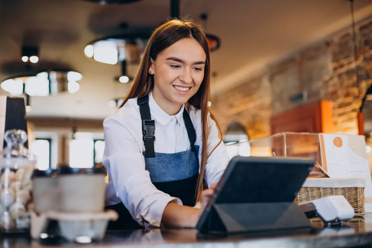 Funcionária de restaurante sorrindo ao usar tablet no balcão, representando a gestão do cardápio com apoio de tecnologia e sistema para restaurantes