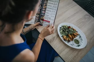 Cliente lendo cardápio impresso ao lado de prato servido, ilustrando o momento de escolha e a importância de um cardápio variado e bem apresentado