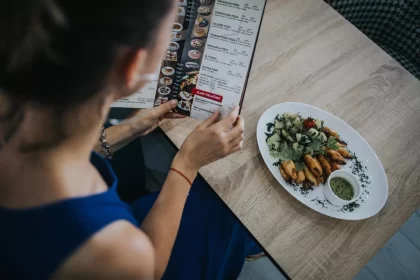 Cliente lendo cardápio impresso ao lado de prato servido, ilustrando o momento de escolha e a importância de um cardápio variado e bem apresentado