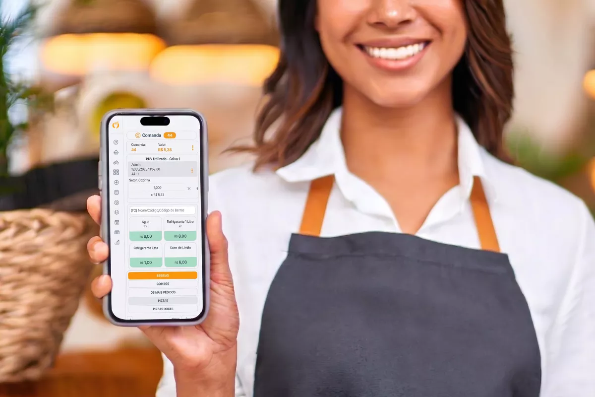 atendente de avental cinza sorrindo e segurando celular com a tela do sistema de comanda eletrônica do ControleNaMão aberta.