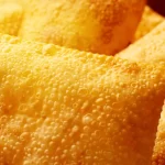Close-up da massa de pastéis fritos recém-saídos do óleo, com superfície dourada e textura crocante cheia de bolhas características da fritura, representando a qualidade do produto final de uma pastelaria