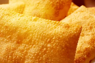 Close-up da massa de pastéis fritos recém-saídos do óleo, com superfície dourada e textura crocante cheia de bolhas características da fritura, representando a qualidade do produto final de uma pastelaria