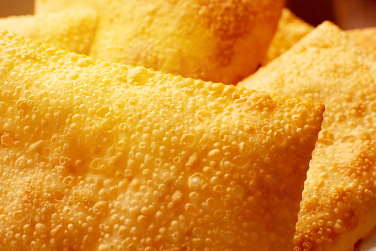Close-up da massa de pastéis fritos recém-saídos do óleo, com superfície dourada e textura crocante cheia de bolhas características da fritura, representando a qualidade do produto final de uma pastelaria