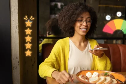 Mulher de óculos e cardigã amarelo sorri enquanto mexe no celular à mesa de restaurante, com prato de comida à frente e ícones de estrelas e medidor de satisfação sobrepostos à imagem